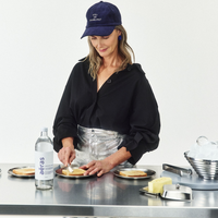 Person preparing food in a kitchen with a bottle of water on the counter.